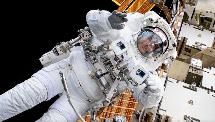 An astronaut in a space suit in outerspace, a space station behind them.