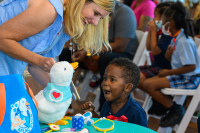 a child sitting at a short table, an adult showing them how the robotic, stuffed duck works