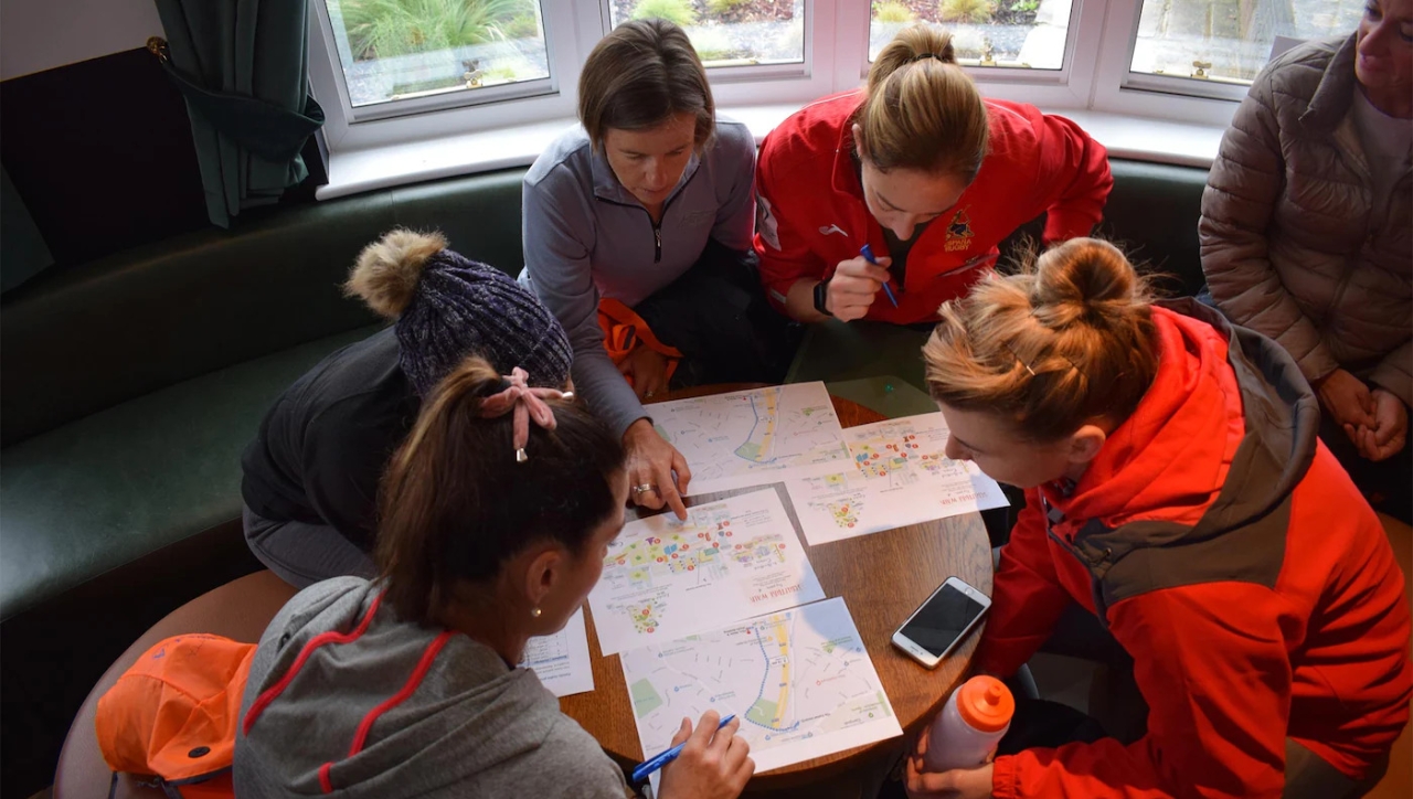 group of five people around a small table looking over maps, and other papers