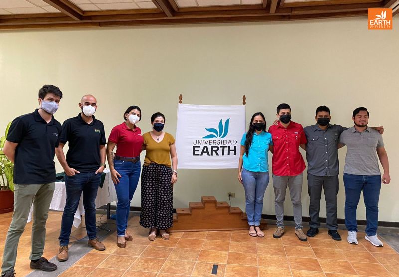 8 people stand in between a Universidad Earth banner.