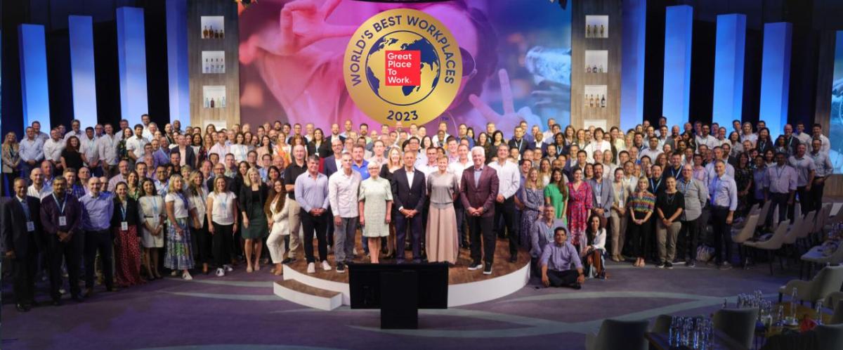 A large group posed on a stage. "World's Best Workplaces" banner above them.