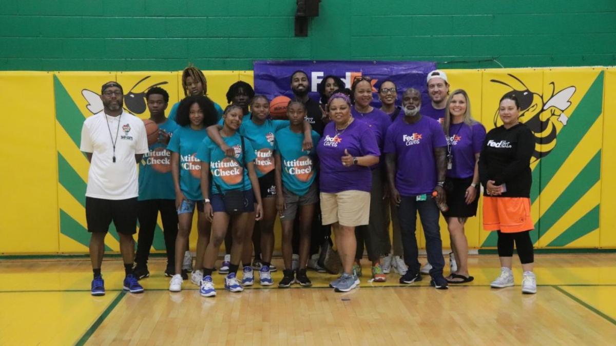 A group of adults and students in gym clothes, posed in a gymnasium.