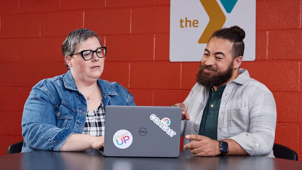 Two people looking at a shared laptop. "The Y" logo on the wall behind them.
