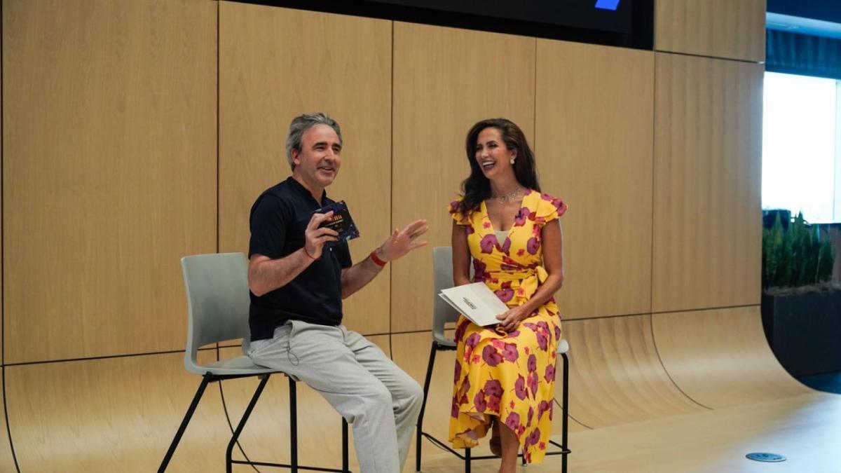 Two people laughing at the front of a room, one with a microphone.