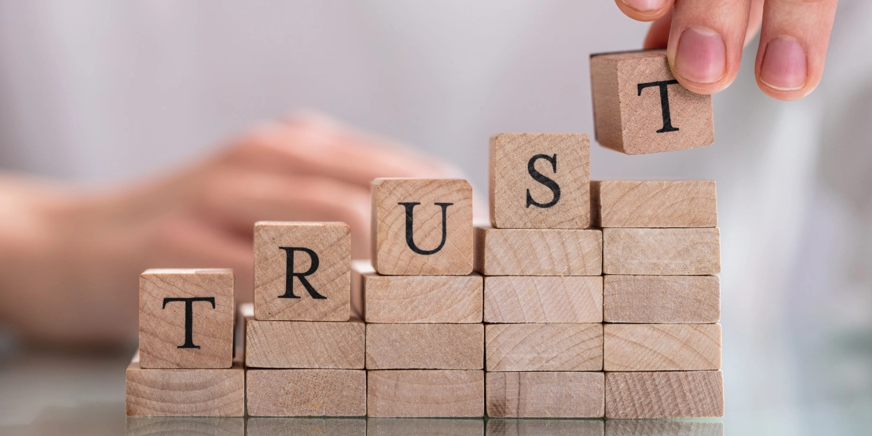 A person stacking wood blocks, the top ones spell out TRUST.