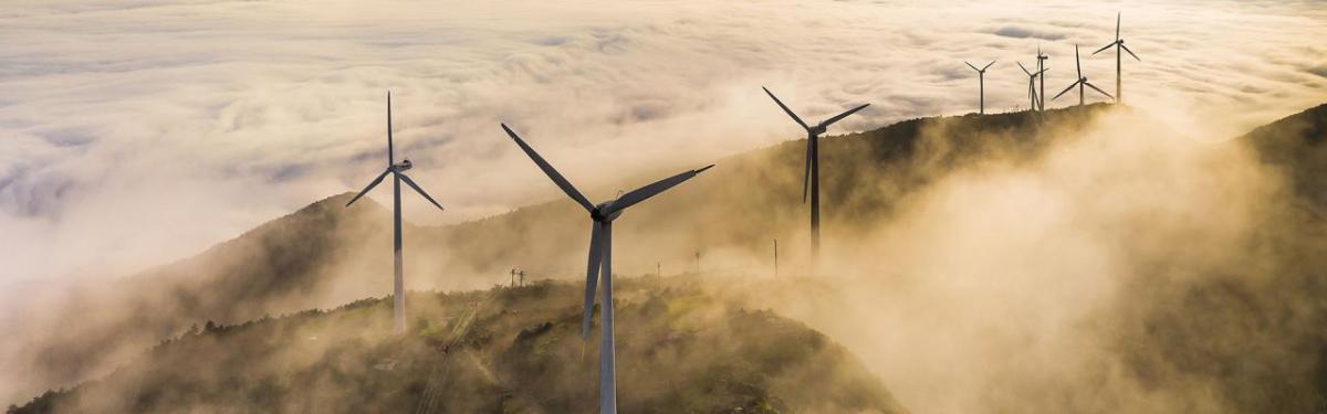 Wind turbines on a high ridge with clouds of fog.