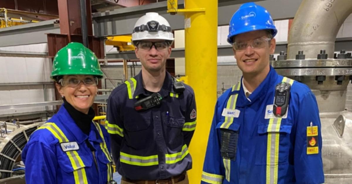 Three people in hard hats, and protective gear standing in an industrial warehouse.