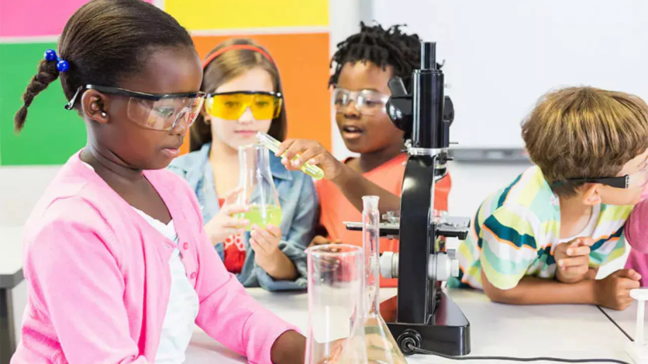 a group of children wearing safety glasses, looking at beakers and test tubes
