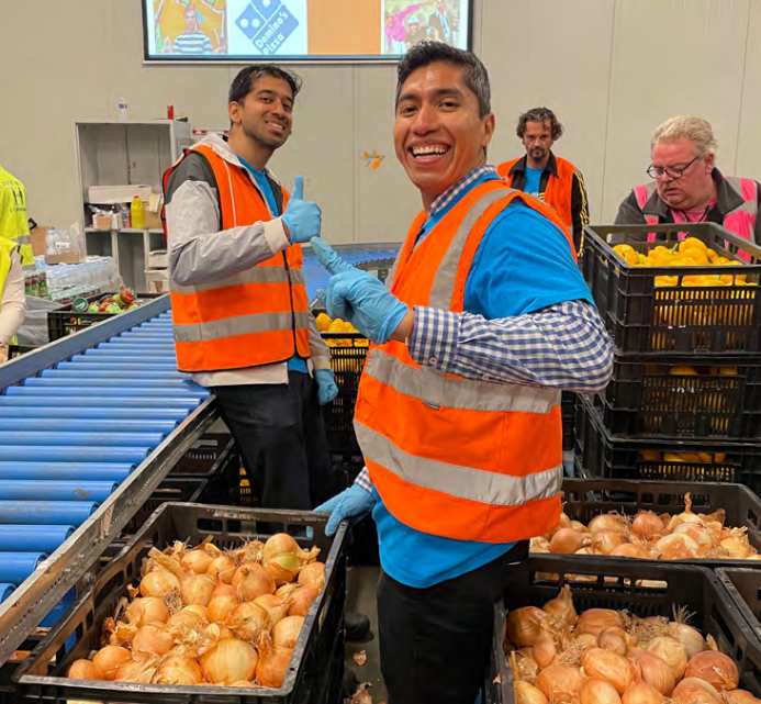 Volunteers with bins of onions, giving thumbs-up to the camera.