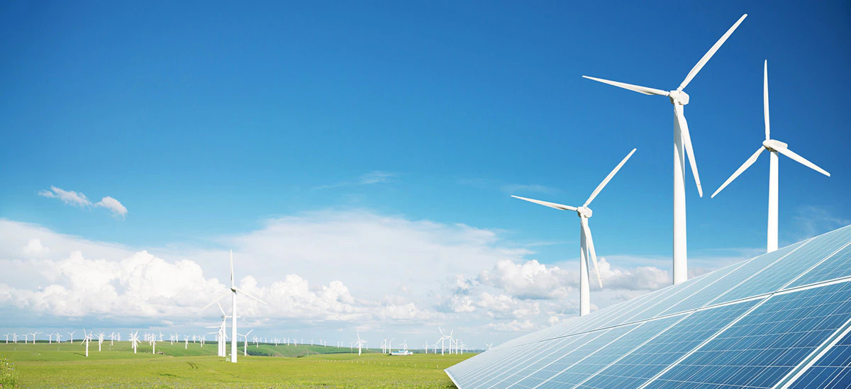 Outside on a bright day, windmills scattered on a large flat plain of grass, a solar panel in the right corner