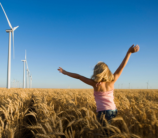 A child running through a crop field. Wind turbines in the distance.