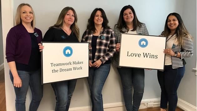 5 women holding signs that read: "Teamwork Makes the Dream Work" and "Love Wins"