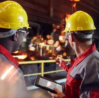 two workers in hard hats look into a facility, one holds an e-device