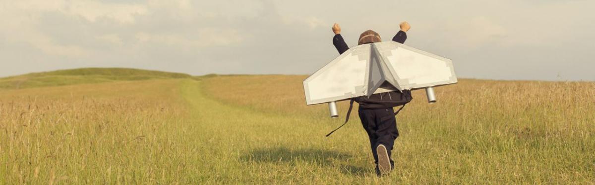 A child running in an open field with arms up and hand built wings attached to their back.