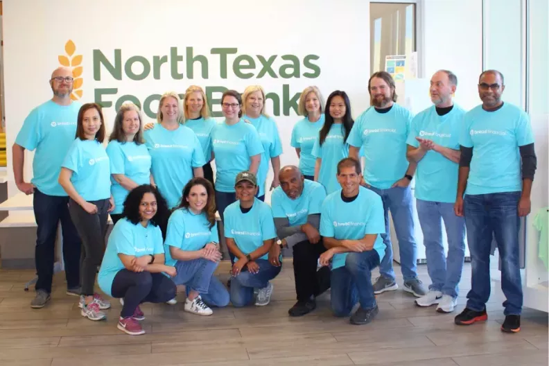 Calvin and a group of others in matching blue &quot;Bread Financial&quot; tshirts, posing in front of a wall with &quot;North Texas Food Bank&quot; on it. 