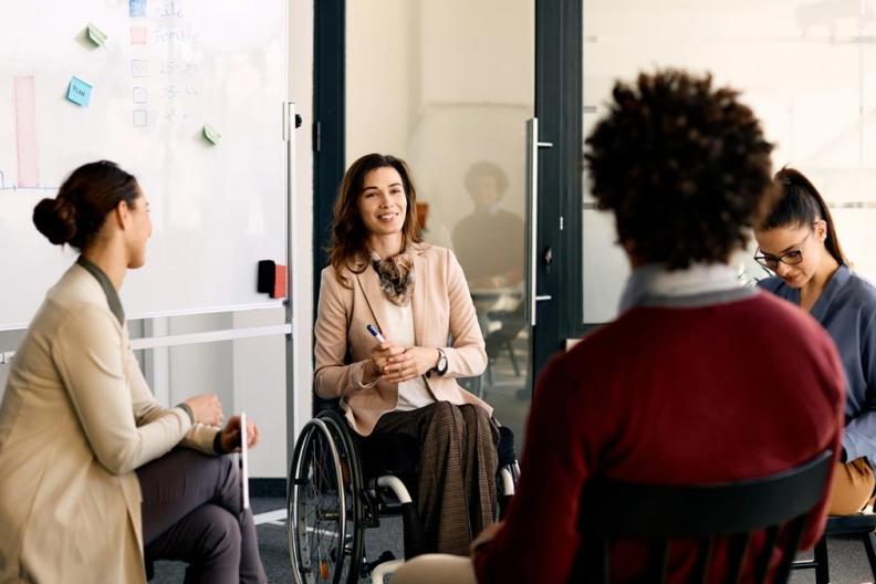 A woman is seated in a wheelchair with three coworkers. 
