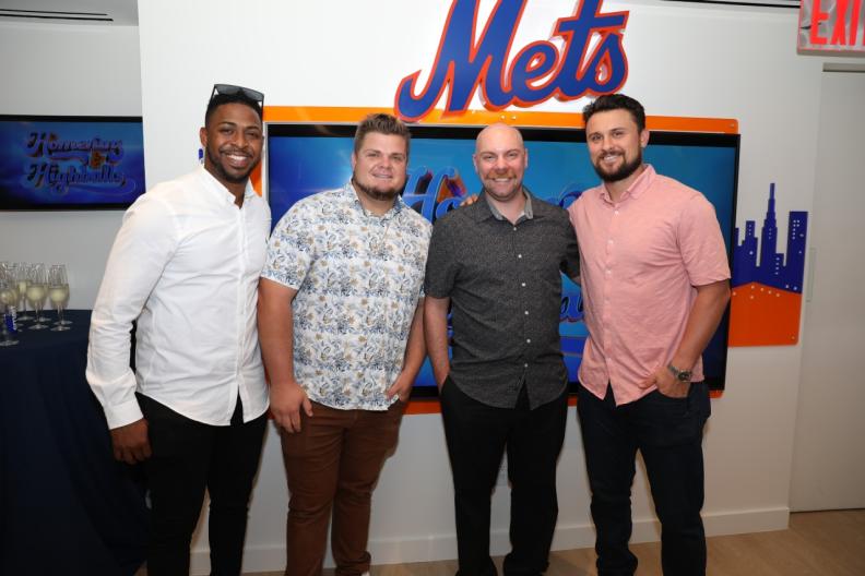Group of four people standing in front of Mets logo 