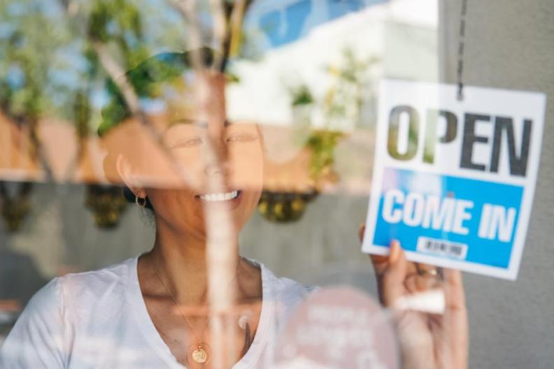Woman in a glass window putting up an Open, Come in sign. 