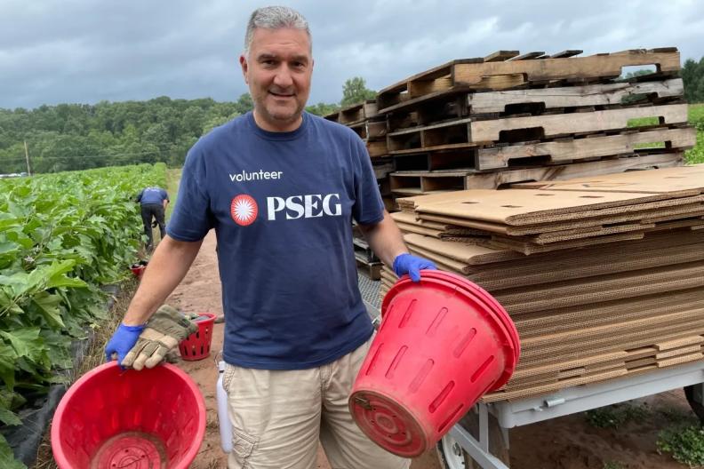 Man wearing a PSEG shirt, outside at a farm holding two large buckets 