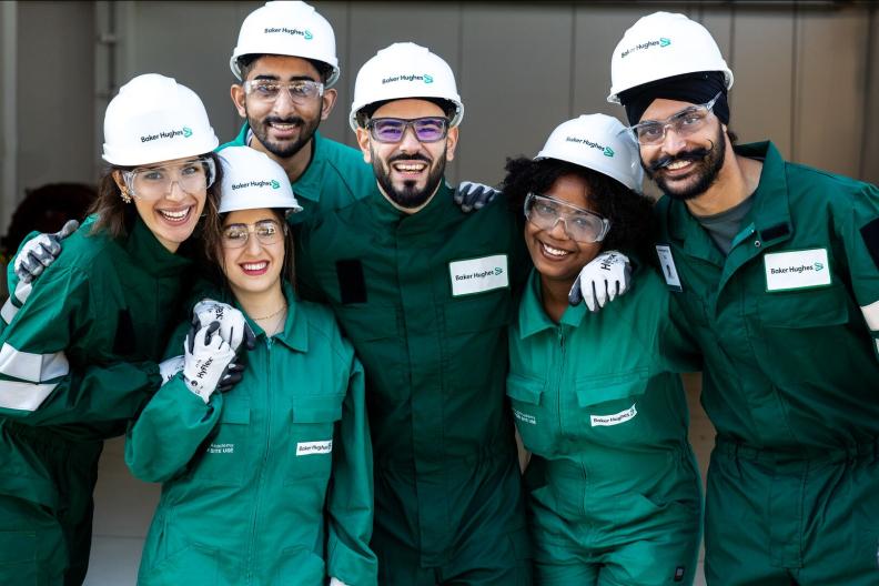 A smiling group of people in Baker Hughes hard hats and green jumpsuits 