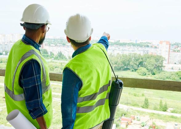 Two workers looking out at a project wearing protective gear.