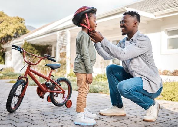 A father helping his son put on his bicycling helmet.