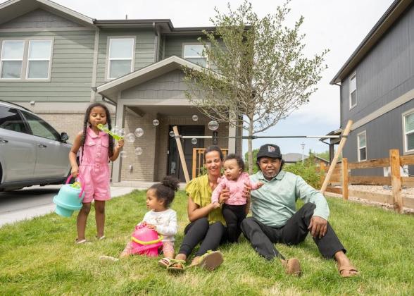 Family of parents and three children sitting in front of house blowing bubbles