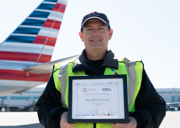 Ken MacTiernan holding a plaque outside, in front of an airplane.