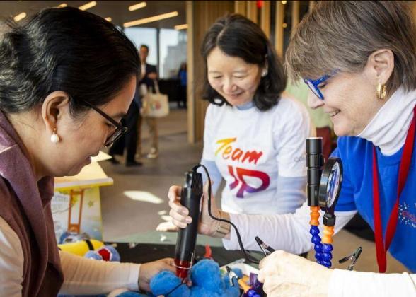 Three people stood around a table helping to modify toys for children with disabilities 