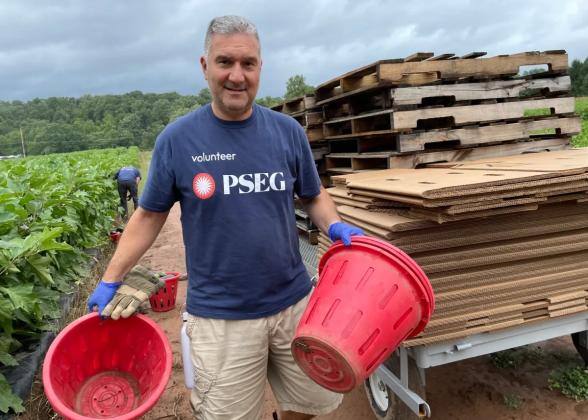 Man wearing a PSEG shirt, outside at a farm holding two large buckets
