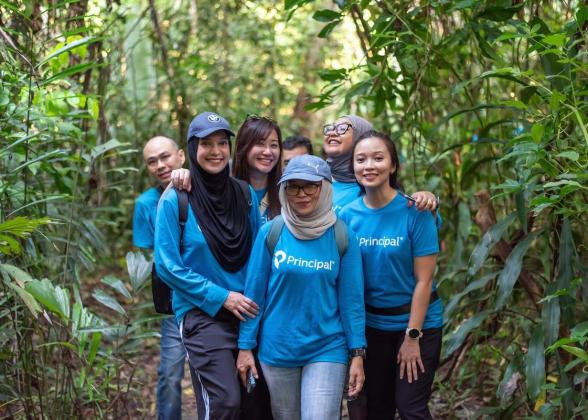 Group of people wearing blue Principal Financial Group shirts in a forest.