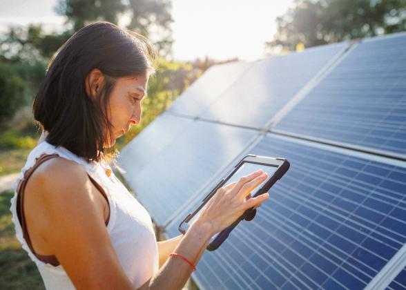 Woman holding a tablet and standing in front of a solar panel array.