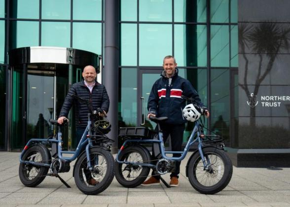 Pete Bowker and Daniel Usher posed by e-bikes outside a Northern Trust building.