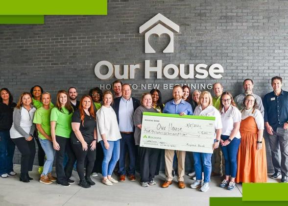 A group of people posed in front of the side of a building &quot;Our House&quot; sign above them. Some holding a large check made to &quot;Our House&quot;.
