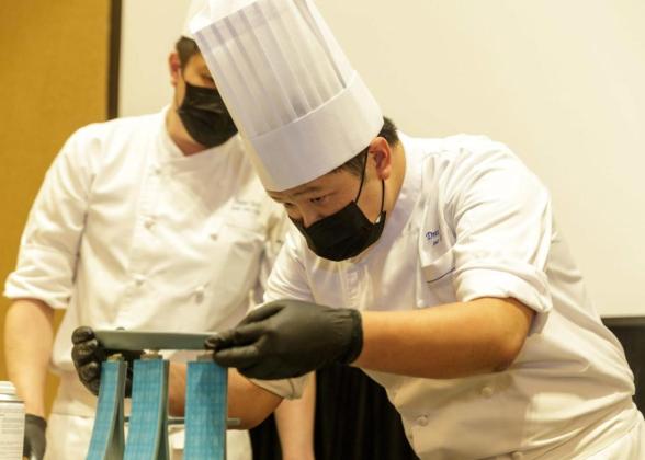 student in a chef&#039;s uniform carefully balancing a plate