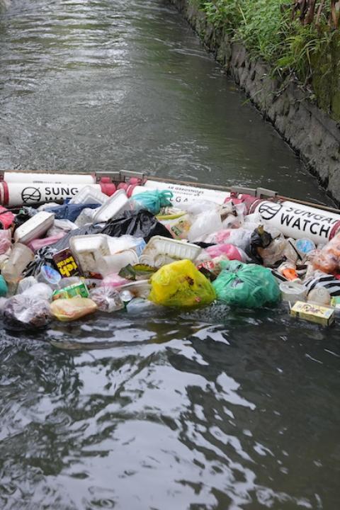 A Sungai Watch trash barrier floats on a river preventing trash from flowing past.