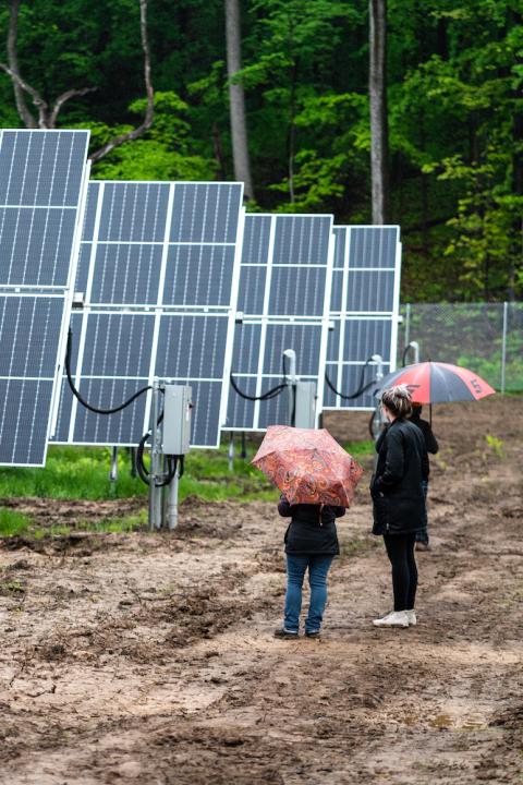 People stand next to a row of solar panels at Lightstar Renewables' project in Saugerties, New York.