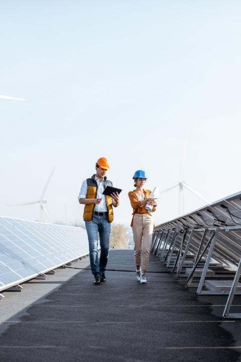 Workers walking through a solar power plant with wind turbines in the background - Achieving the SDGs with renewable energy