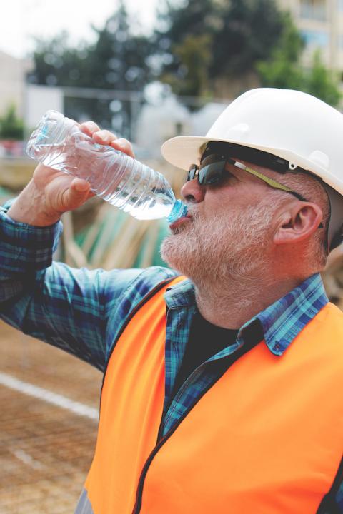 construction worker taking a water break while working outside on a hot day - preventing heat-related illness at work