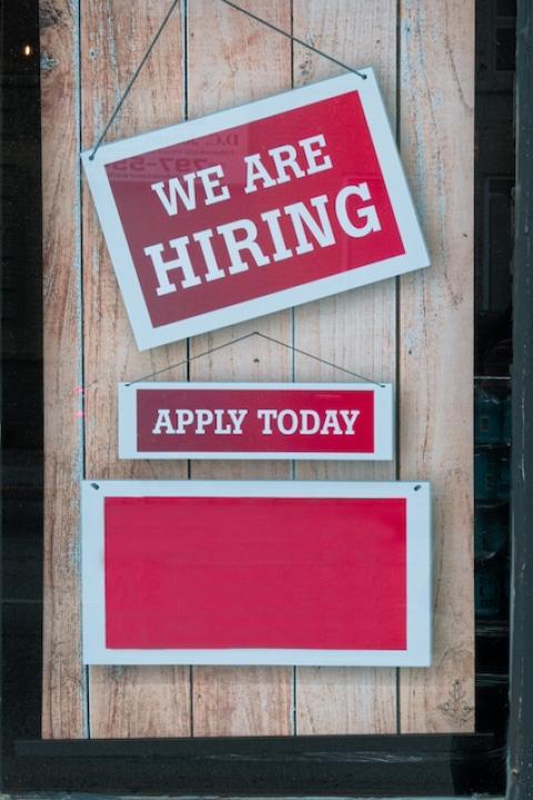 "We are hiring" sign hanging on a door. 
