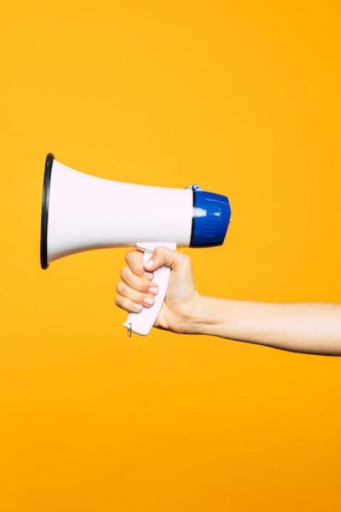 hand holding megaphone against yellow background - the top ESG issues brands should speak out on in 2024