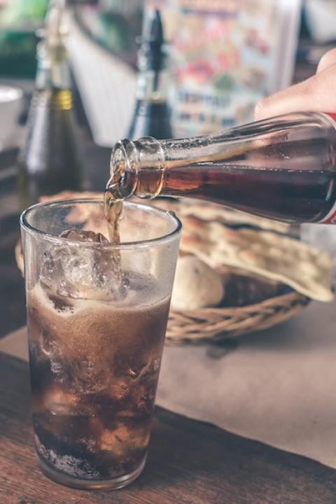 hand pouring coca-cola from a glass bottle at a restaurant table - coca-cola sells billions of beverages in refillable packaging made from plastic and glass globally