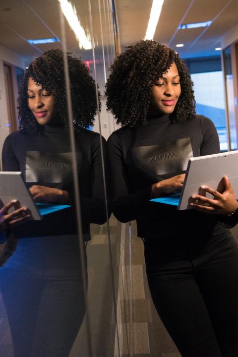 A photo of a woman and her reflection working on a laptop - soft skills for tech leaders