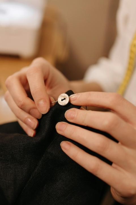 A person sewing a button onto a piece of clothing. 
