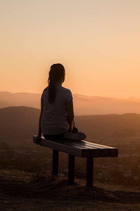 woman sitting meditating on park bench with mountain view at sunset