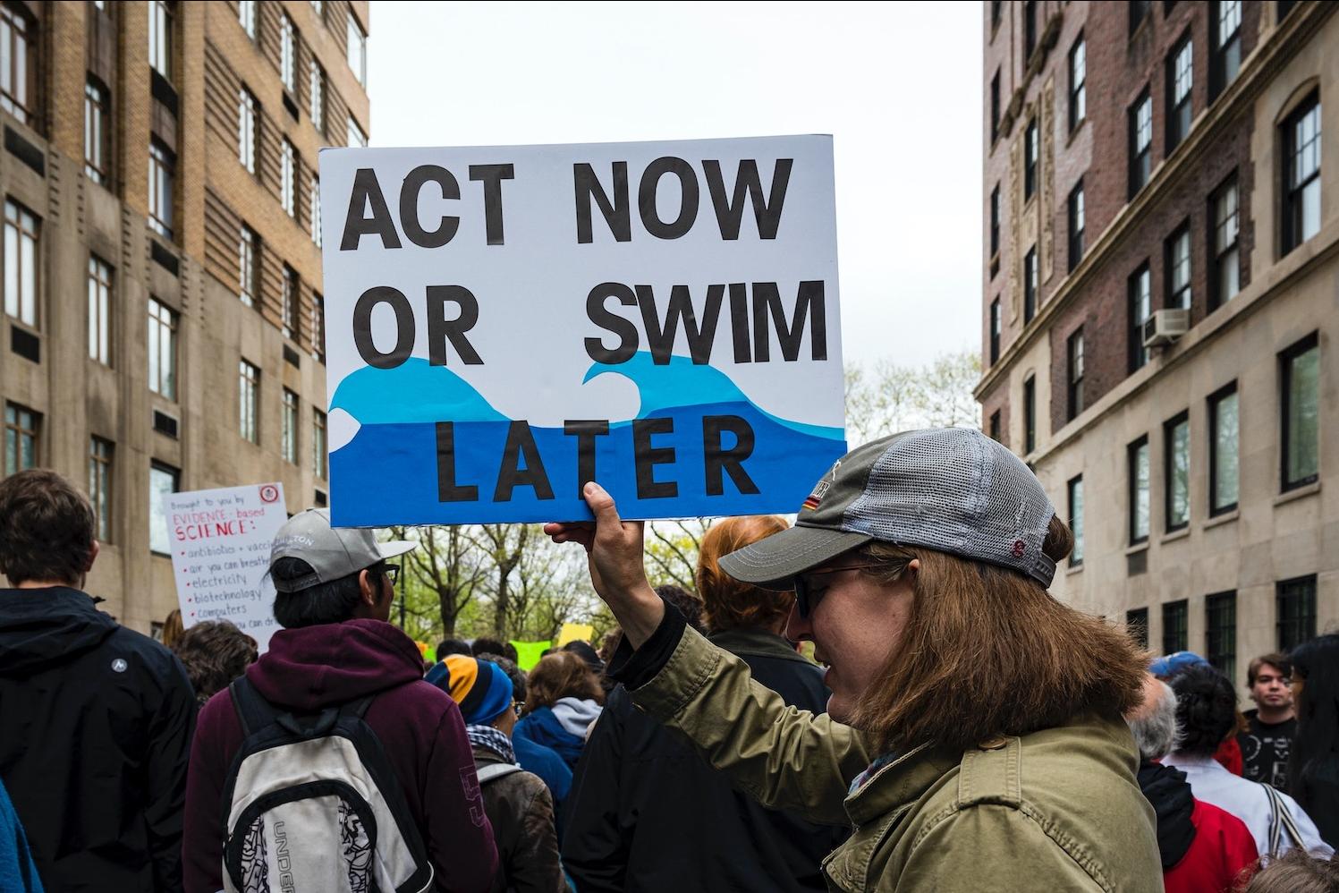 limate protester holding sign that says act now or swim later - net-zero emissions