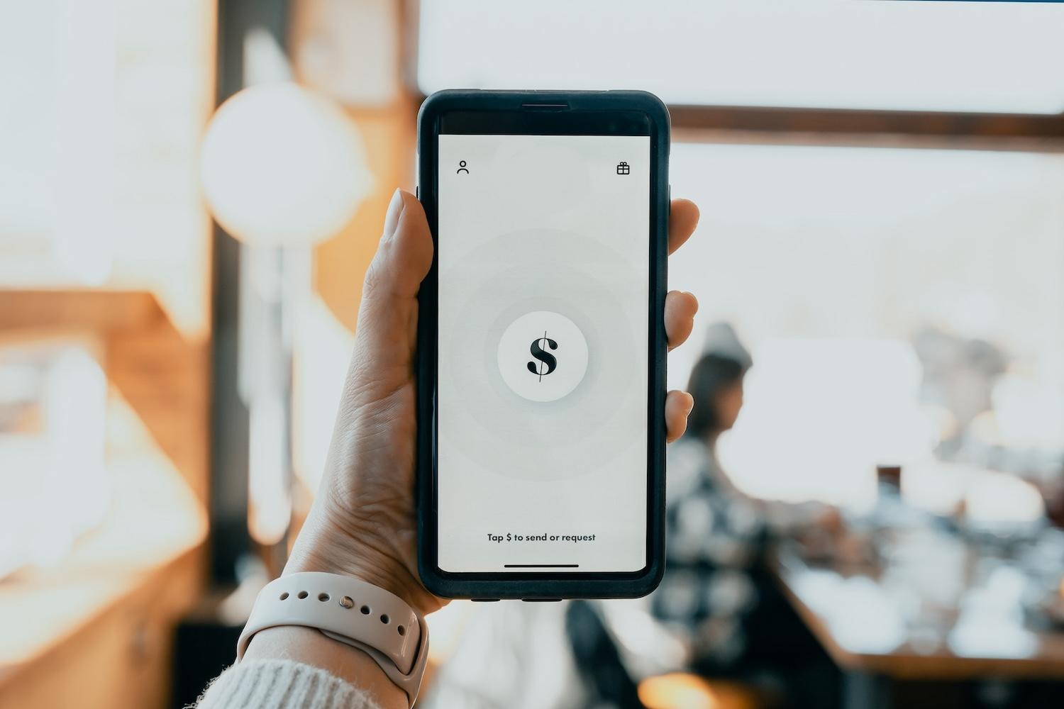 Person holding smartphone with dollar sign on the screen - the $17 billion cost of sustainability brand switching for financial companies