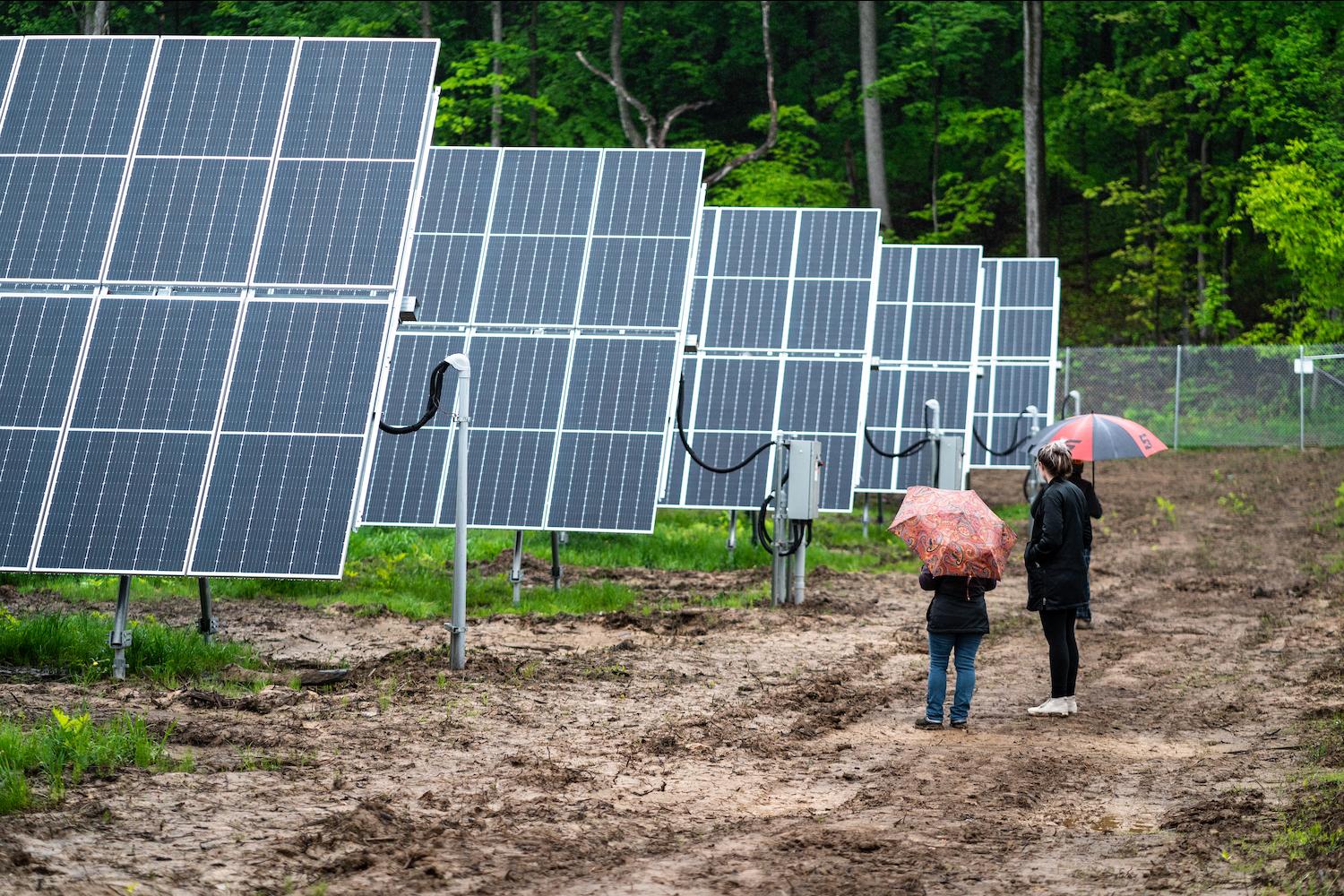 People stand next to a row of solar panels at Lightstar Renewables' project in Saugerties, New York.