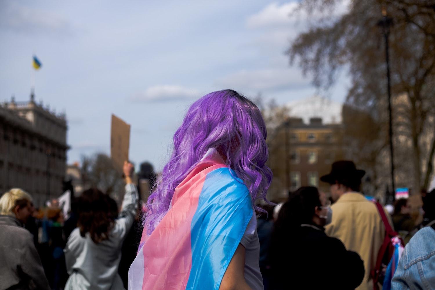 Woman with purple hair at protest wearing transgender flag 