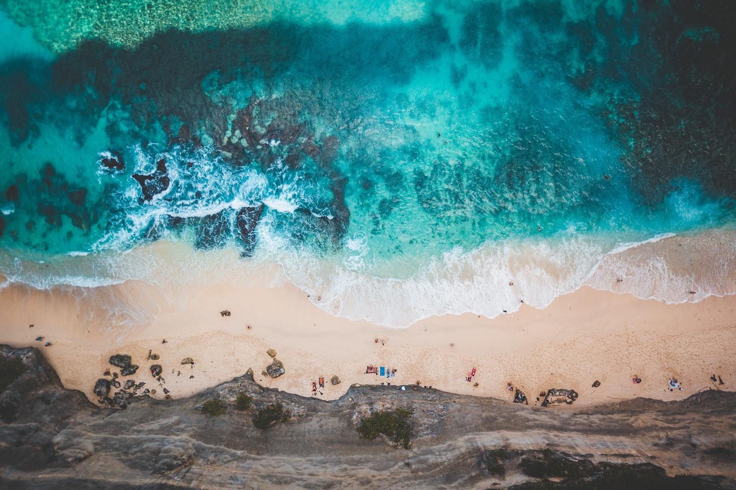 aerial view of ocean crashing on a beach shoreline - rising marine temperatures threaten ocean life